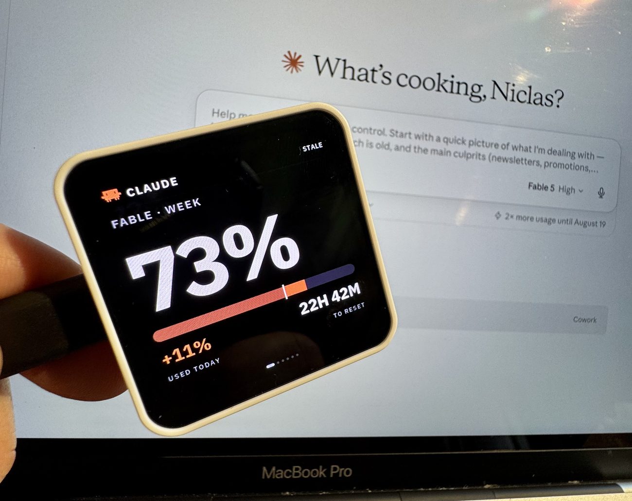 The panel held in a hand showing Claude's weekly quota at 73 percent, 22 hours 42 minutes to reset