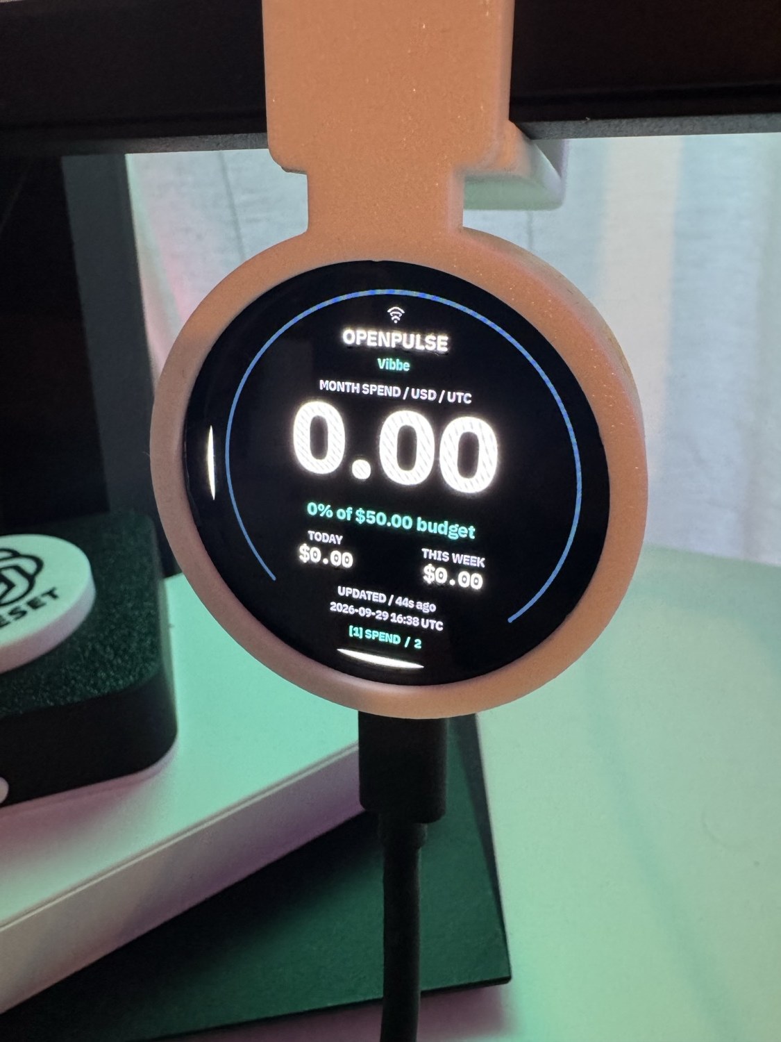 Owner’s round VibePulse display in a pink enclosure showing the OpenPulse monthly API spend page