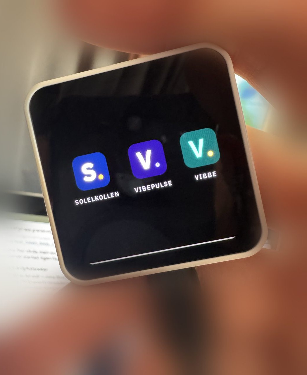 Photo of the device held in hand, its screen showing the launcher with app tiles for Solelkollen, VibePulse and Vibbe